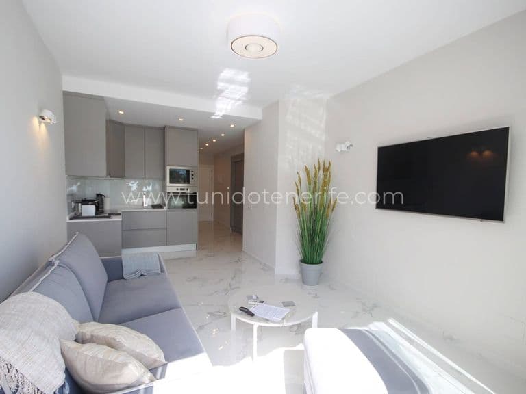 Bright modern living room with gray sofa, TV and open kitchen in background