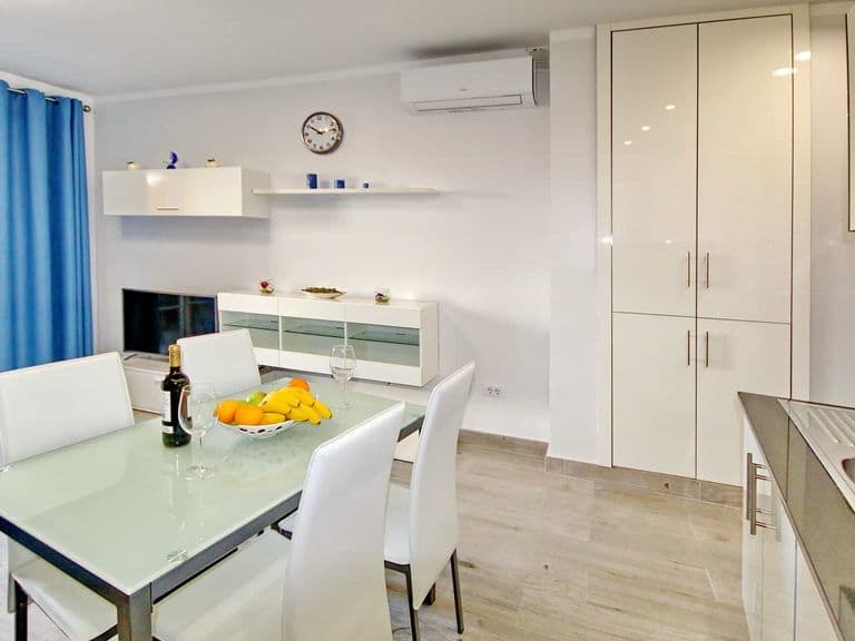 Luminoso zona pranzo con tavolo in vetro, sedie bianche e armadio alto