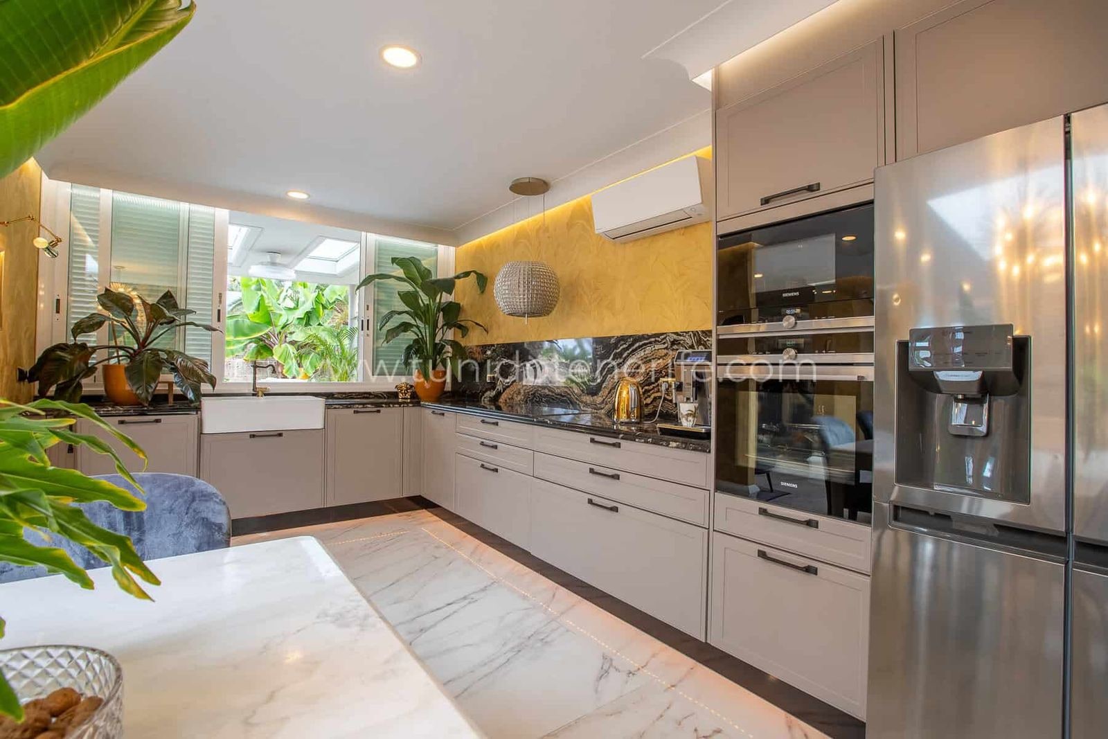 Cocina moderna con armarios blancos, encimera de mármol y electrodomésticos de acero