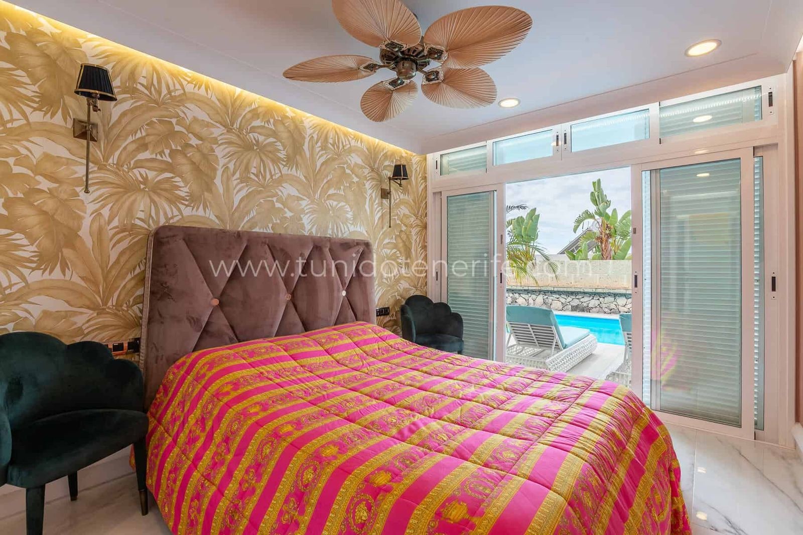 Dormitorio con cama, palmeras decorativas y acceso a la piscina