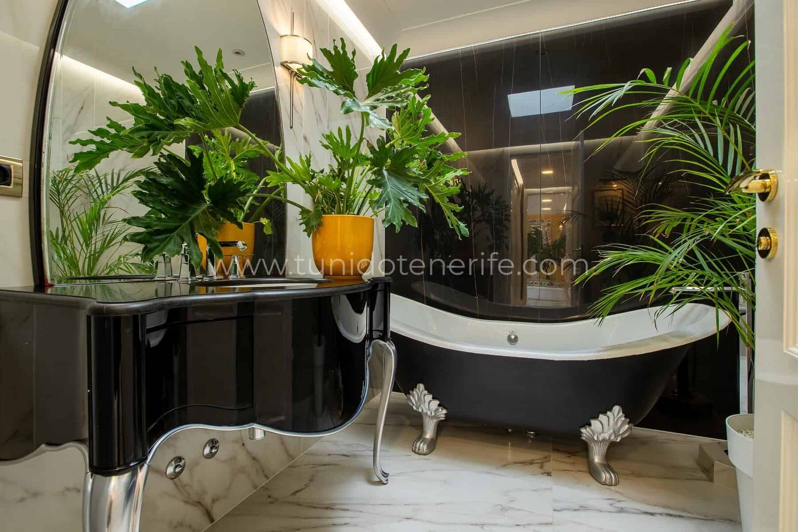 Baño moderno con bañera negra, lavabo y plantas decorativas