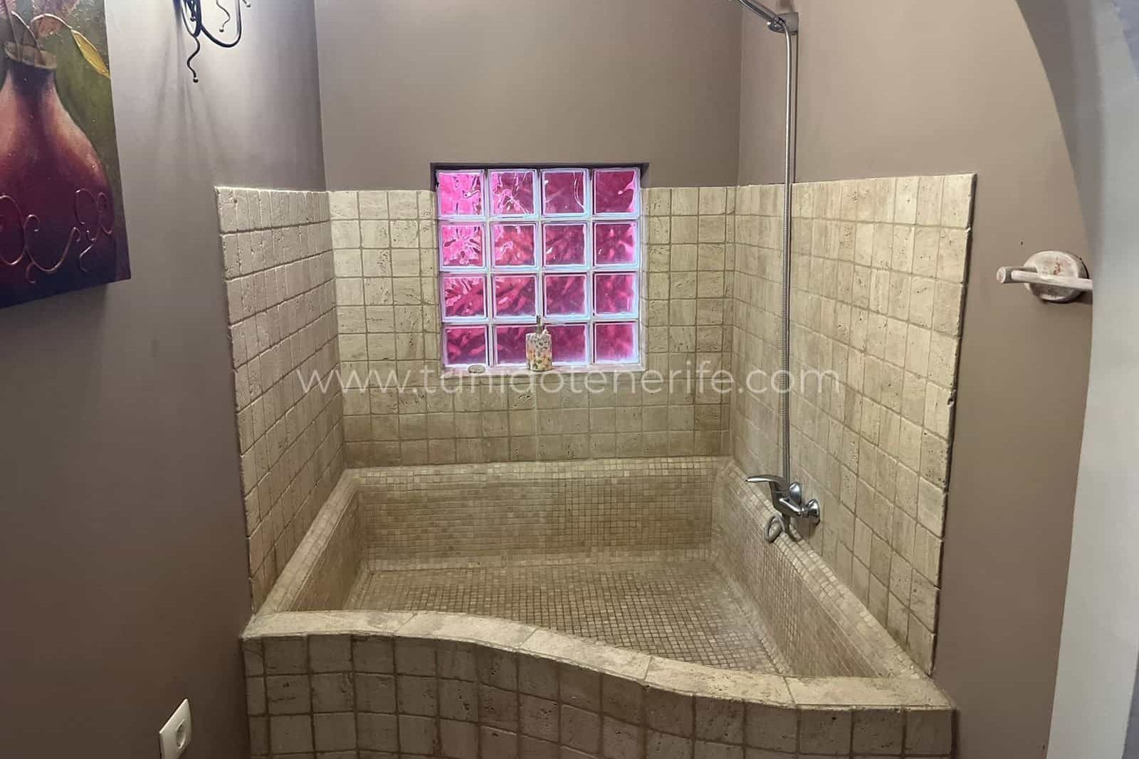 Walk-in shower with beige tiles and small glass window