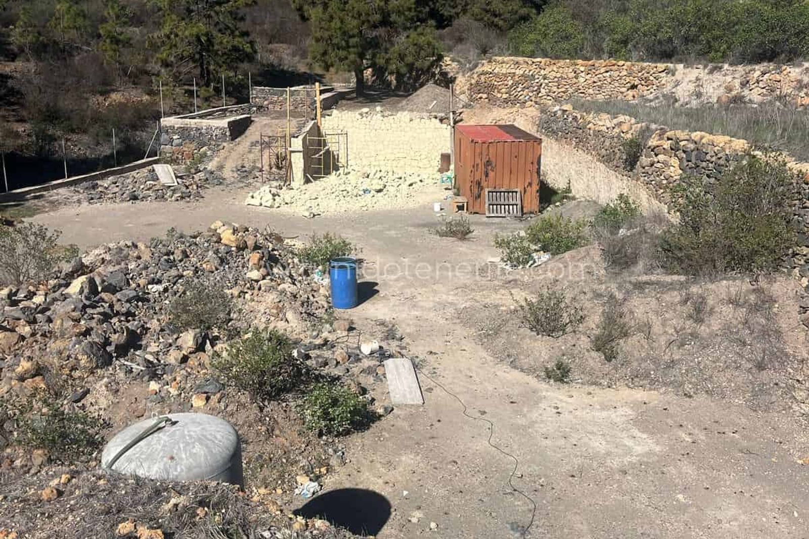 Outdoor lot with rubble, barrels and a small construction shed