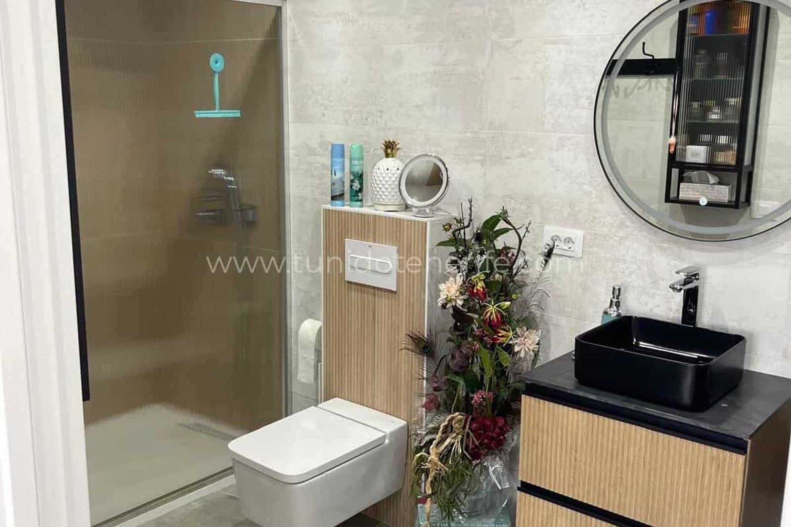 Baie modernă cu duș din sticlă, chiuvetă neagră și decor floral