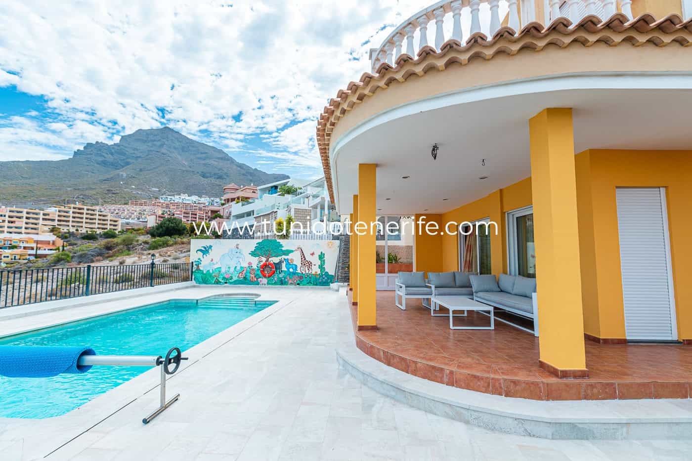 Terrasse couverte au bord de la piscine avec canapé d’extérieur et colonnes jaunes.