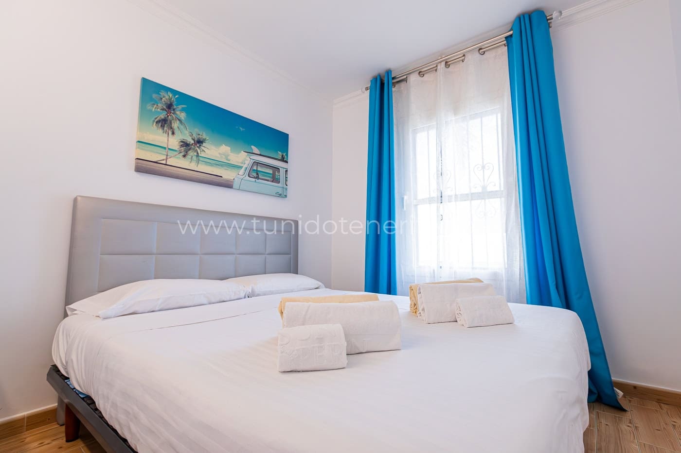 Camera luminosa con letto matrimoniale, tende blu e quadro tropicale