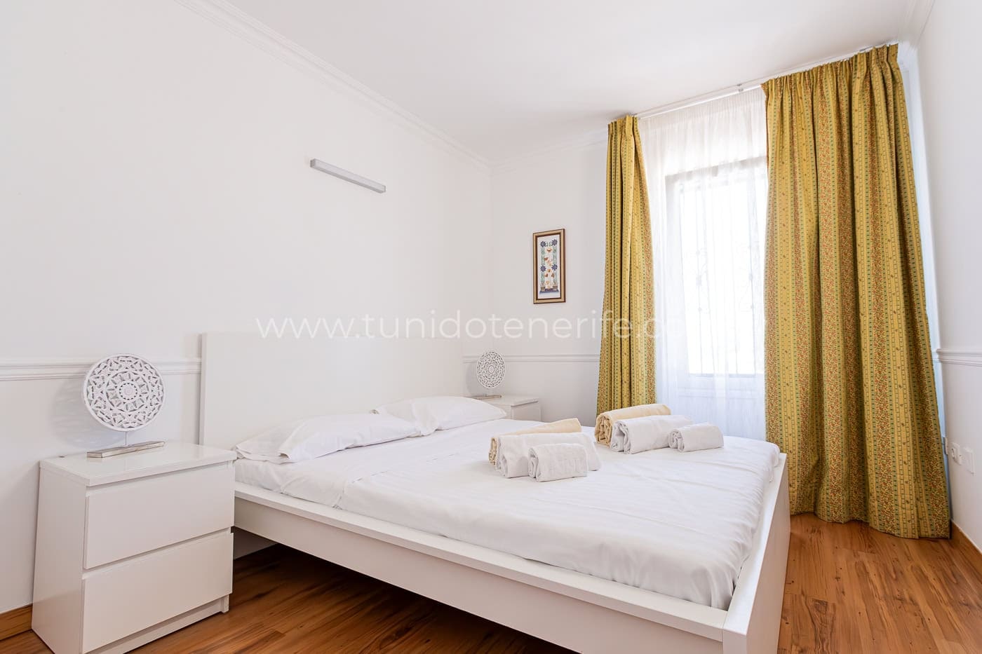 Camera da letto luminosa con letto bianco e tende senape