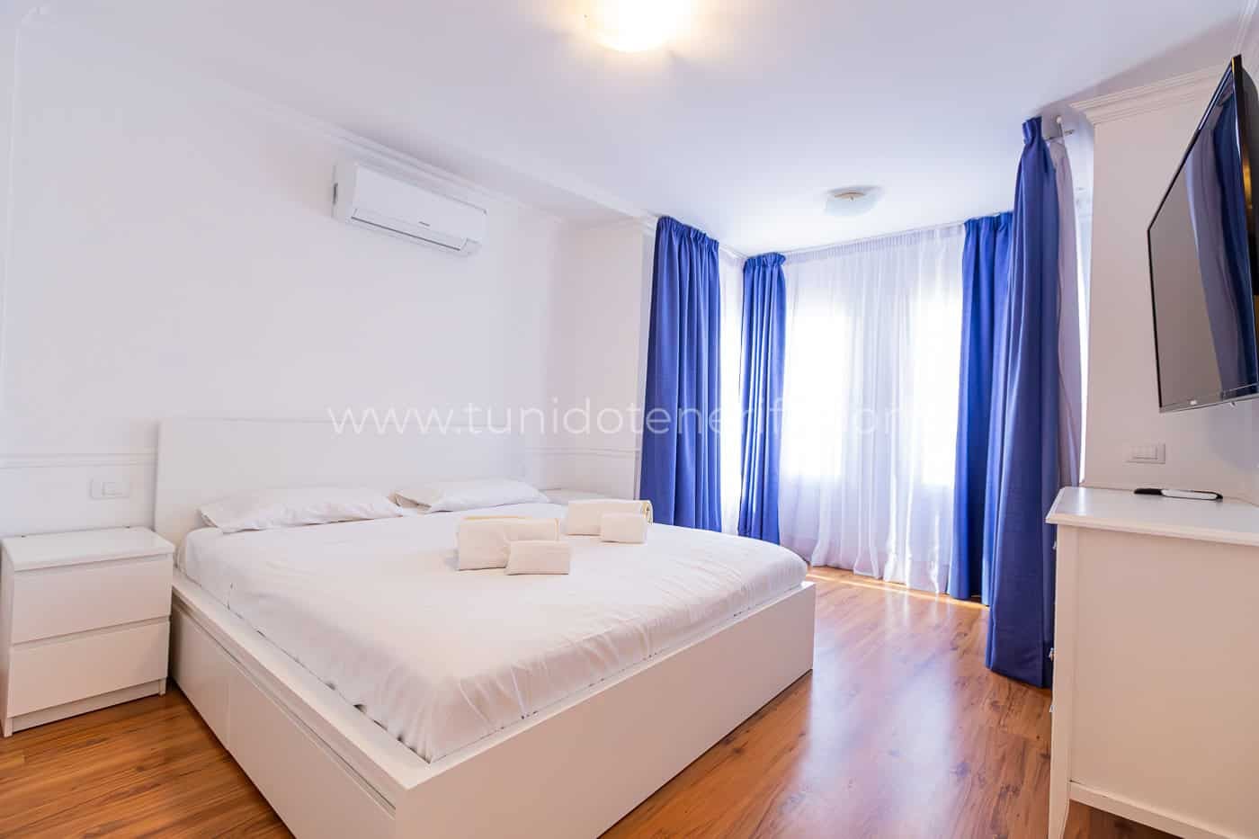 Camera da letto luminosa con letto matrimoniale, tende blu e armadio bianco