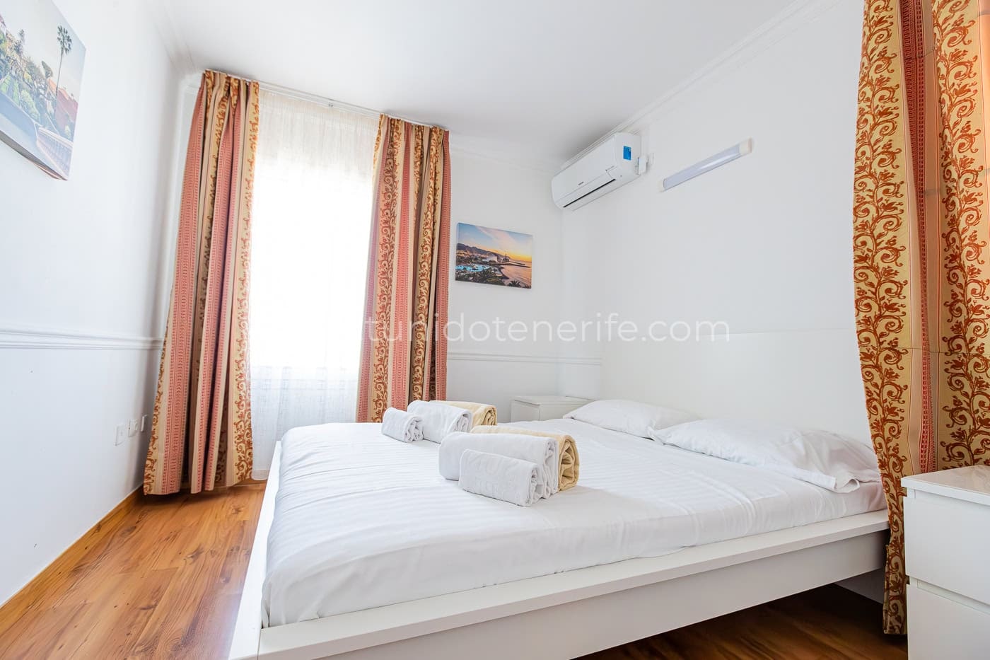 Camera da letto luminosa con letto matrimoniale, tende e pavimento in legno
