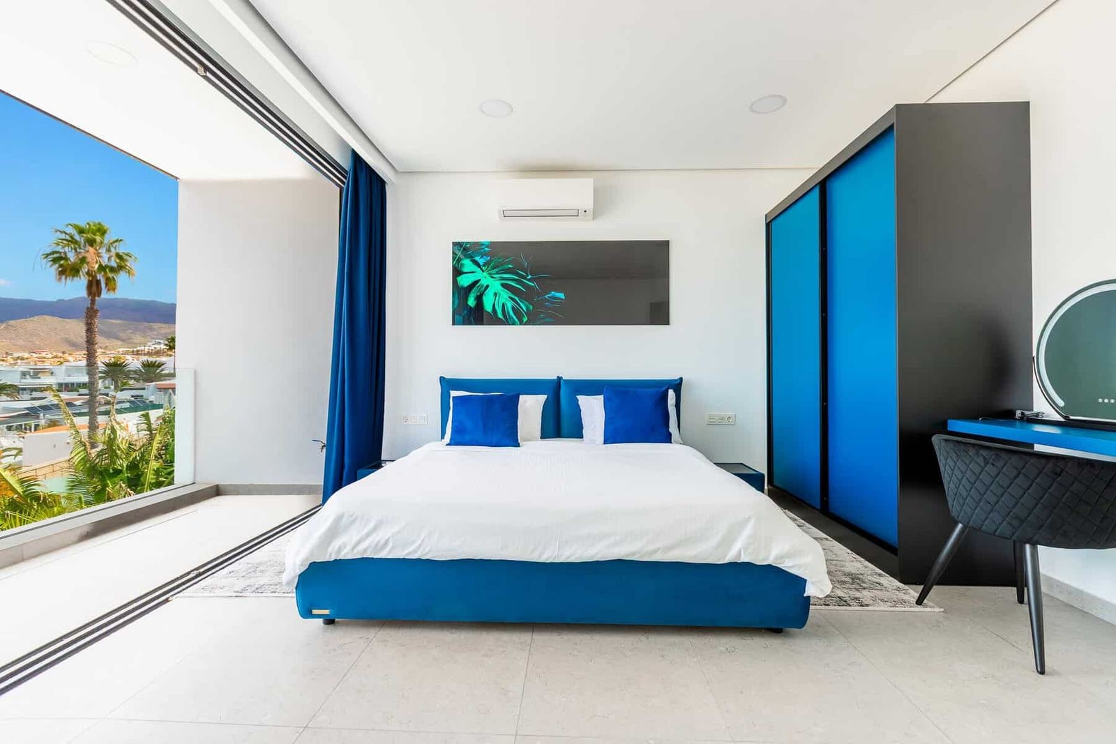 Dormitorio moderno con cama azul, escritorio y gran ventanal