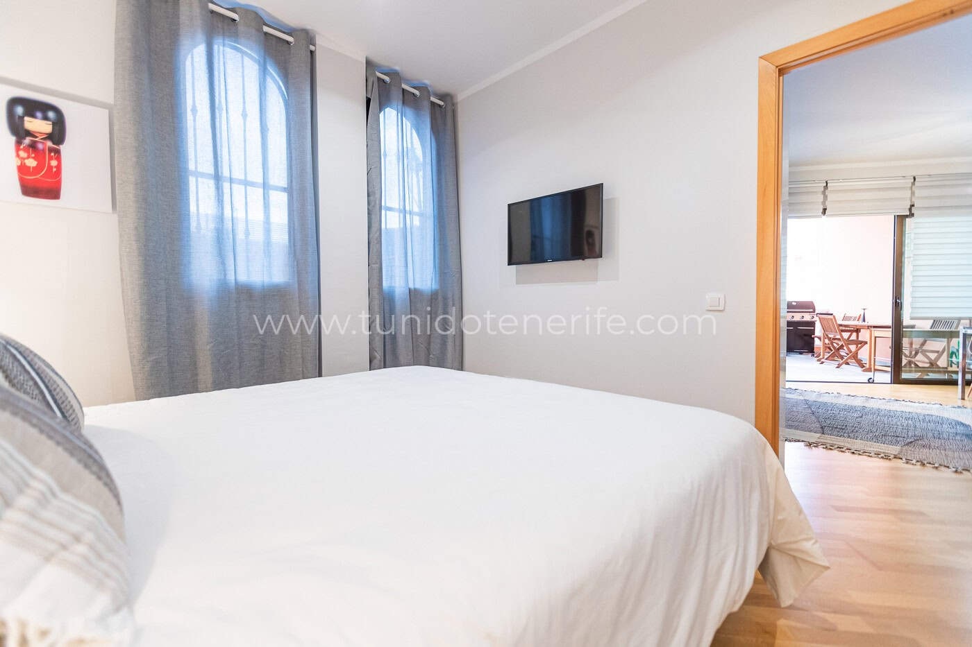 Dormitorio luminoso con cama doble, cortinas grises y televisor