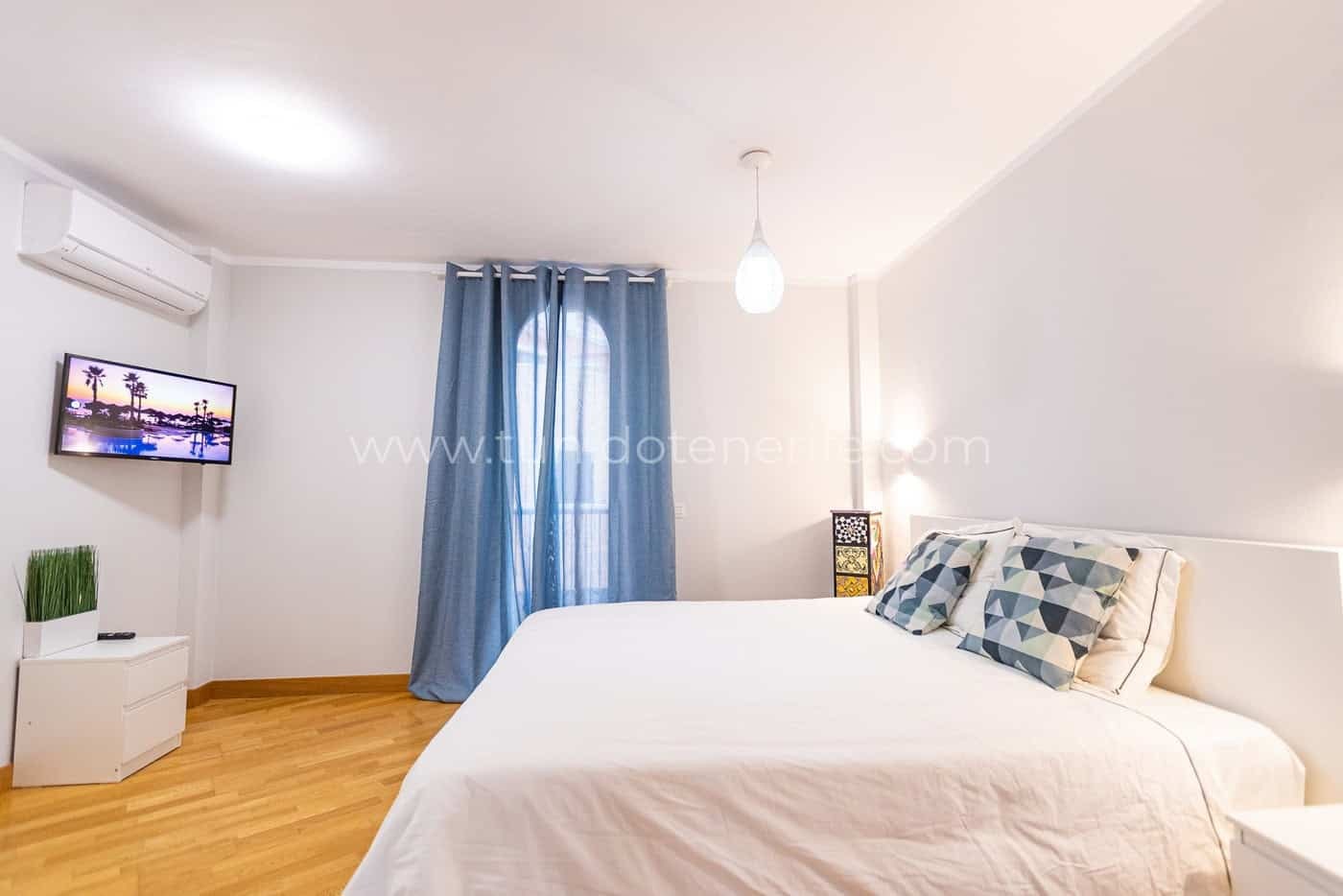 Dormitorio luminoso con cama doble, cortinas azules y suelo de madera
