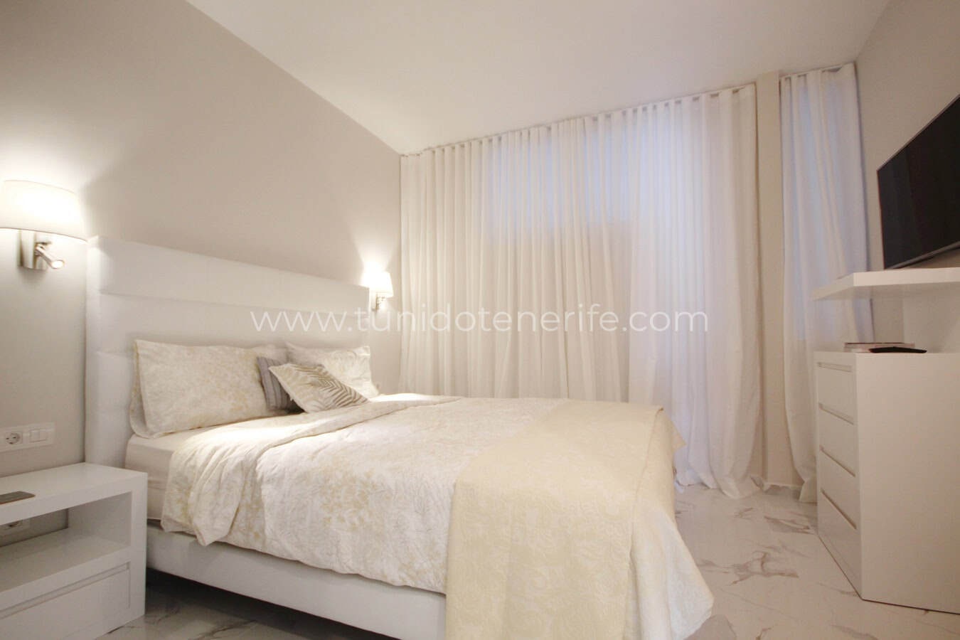 Bright bedroom with double bed, white curtains and bedside tables