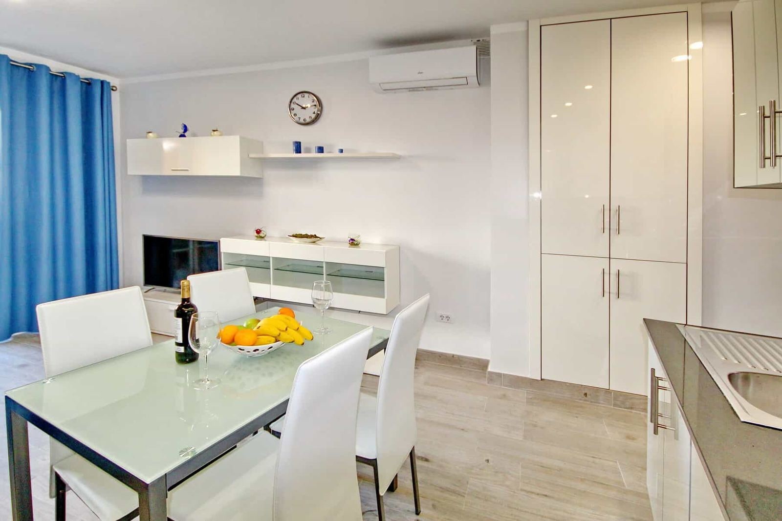 Luminoso zona pranzo con tavolo in vetro, sedie bianche e armadio alto
