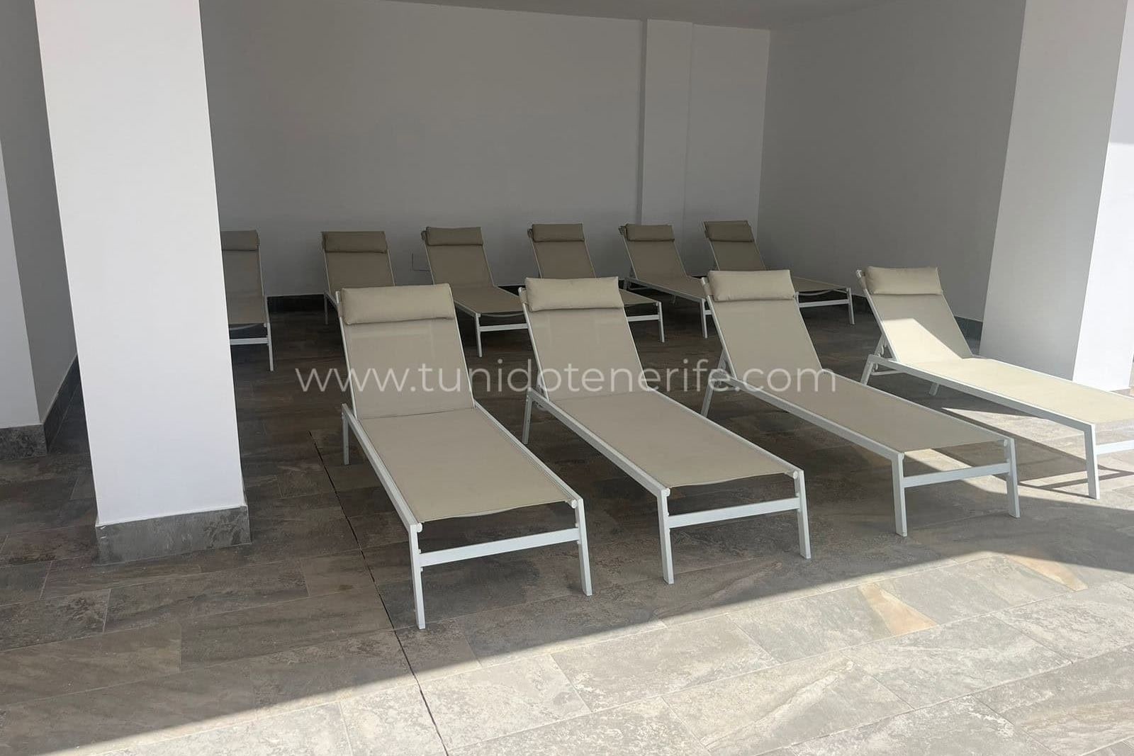 Tumbonas beige alineadas bajo una zona cubierta