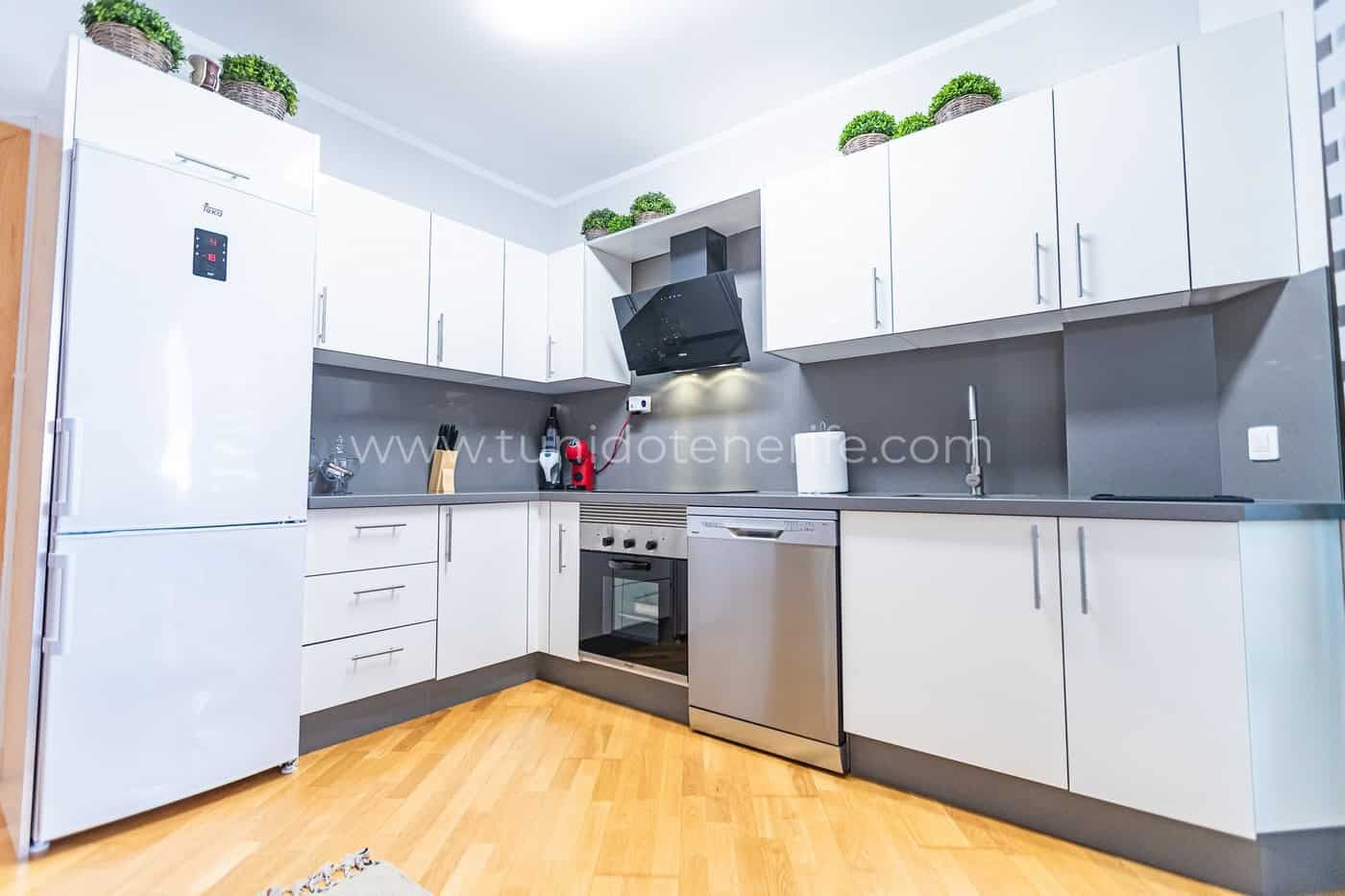Cocina moderna blanca con electrodomésticos integrados y suelo de madera