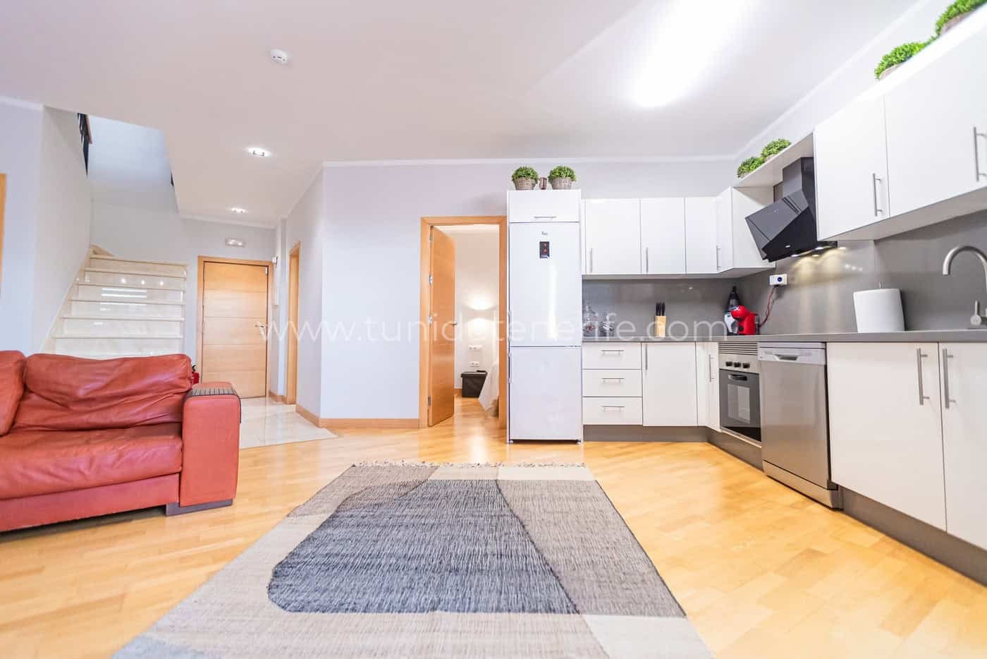 Salón con cocina abierta, sofá rojo y suelo de madera