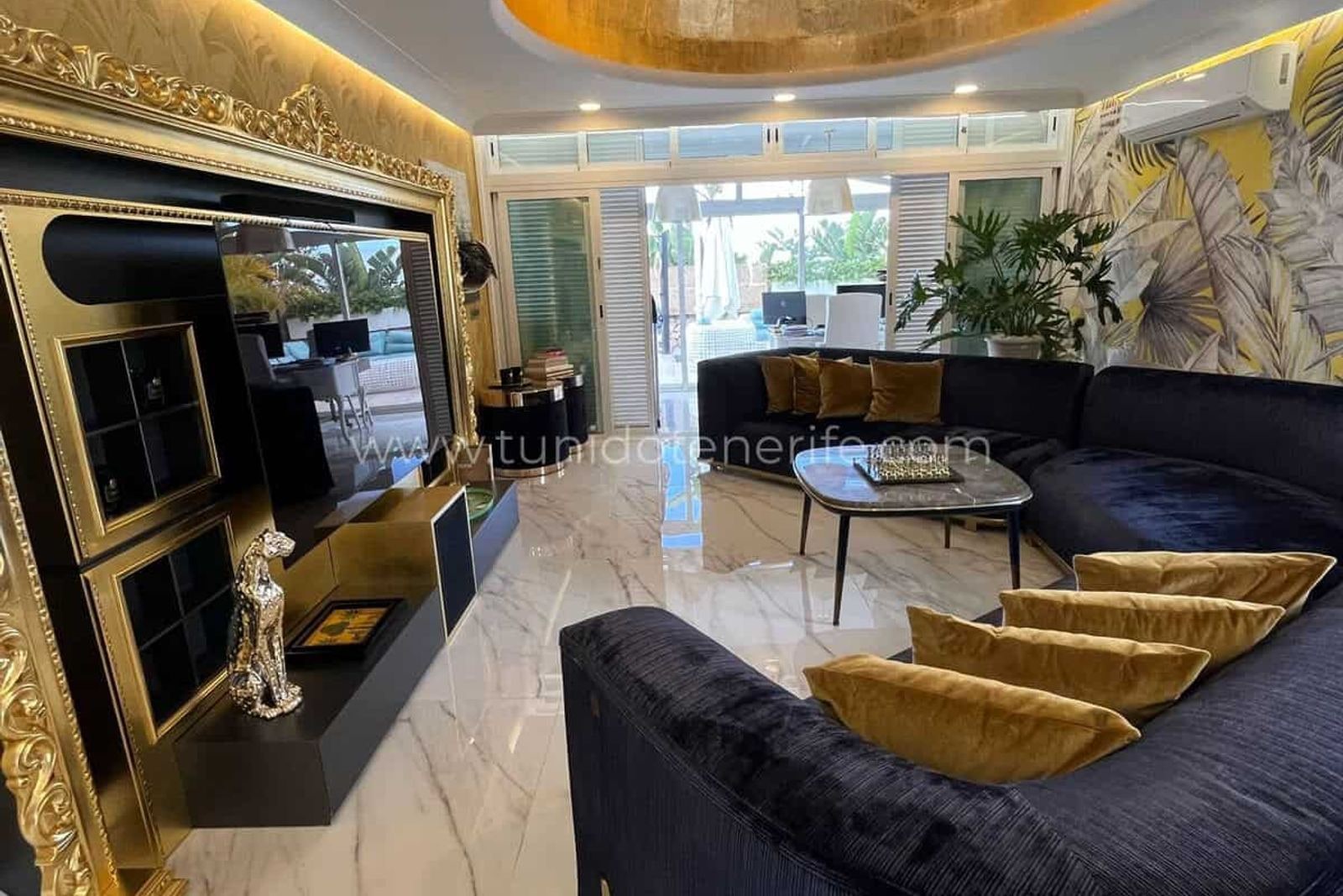 Salón con sofá negro, mesa de centro y mueble de TV dorado