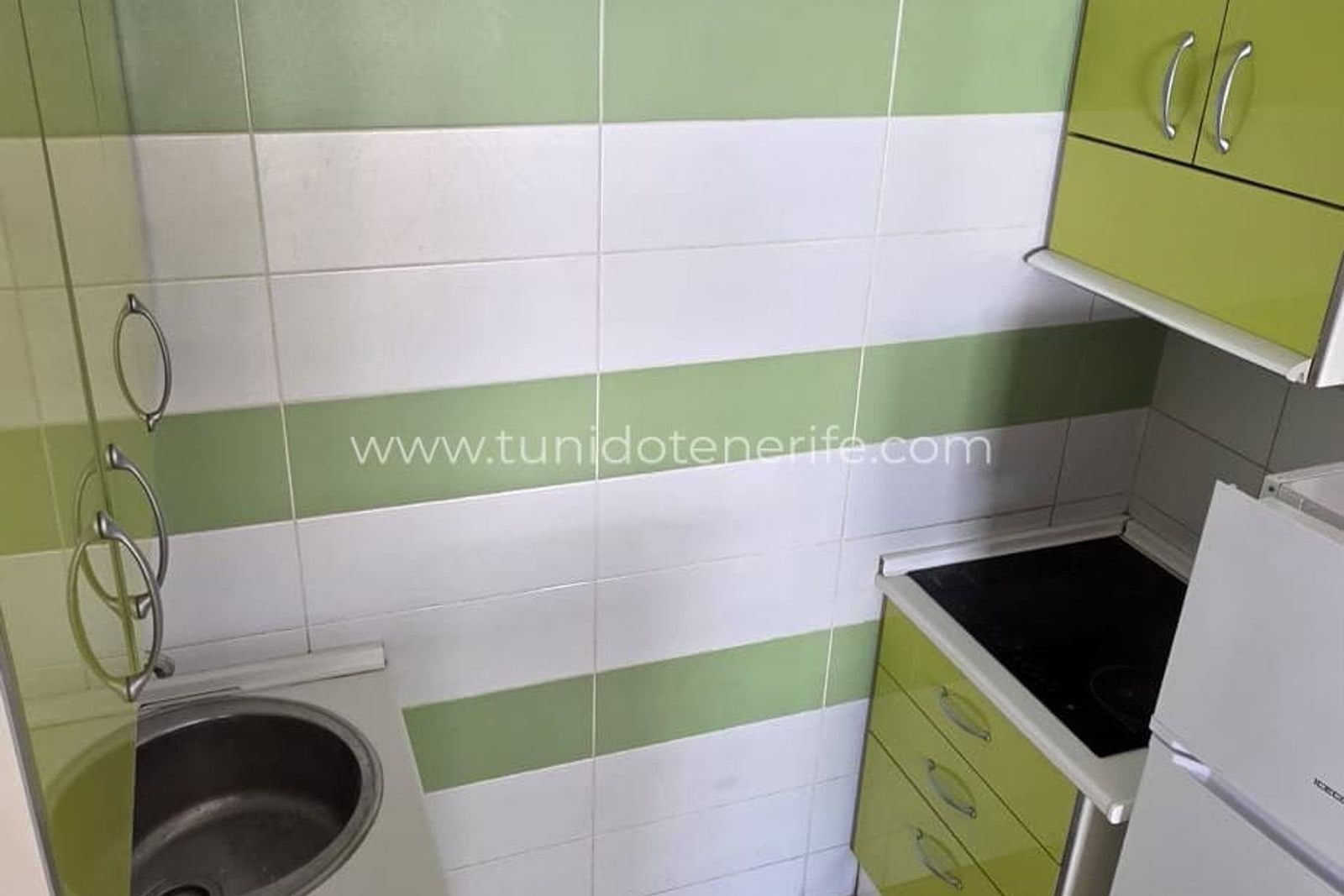 Cocina compacta con muebles verdes y azulejos blancos y verdes