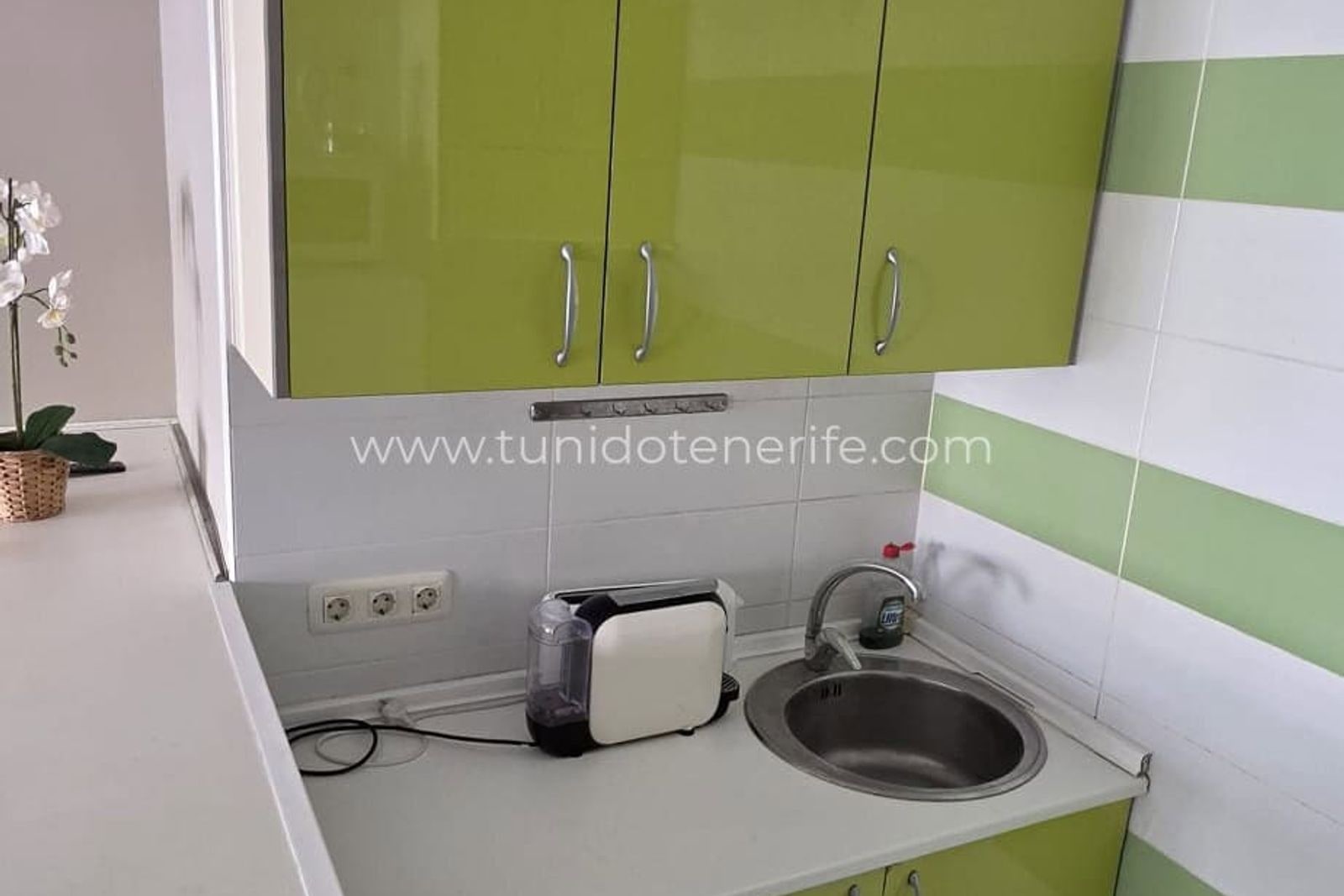 Cocina con muebles verdes, fregadero y tostadora sobre la encimera