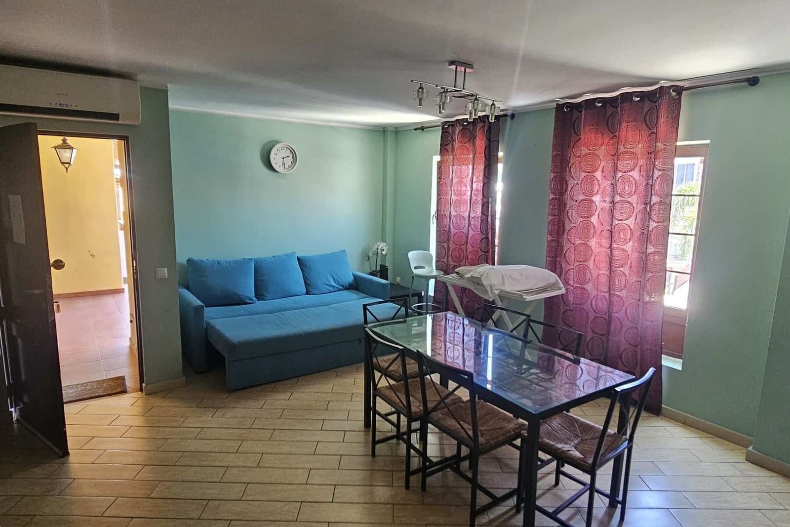 Salón con sofá azul, mesa de comedor y cortinas granates