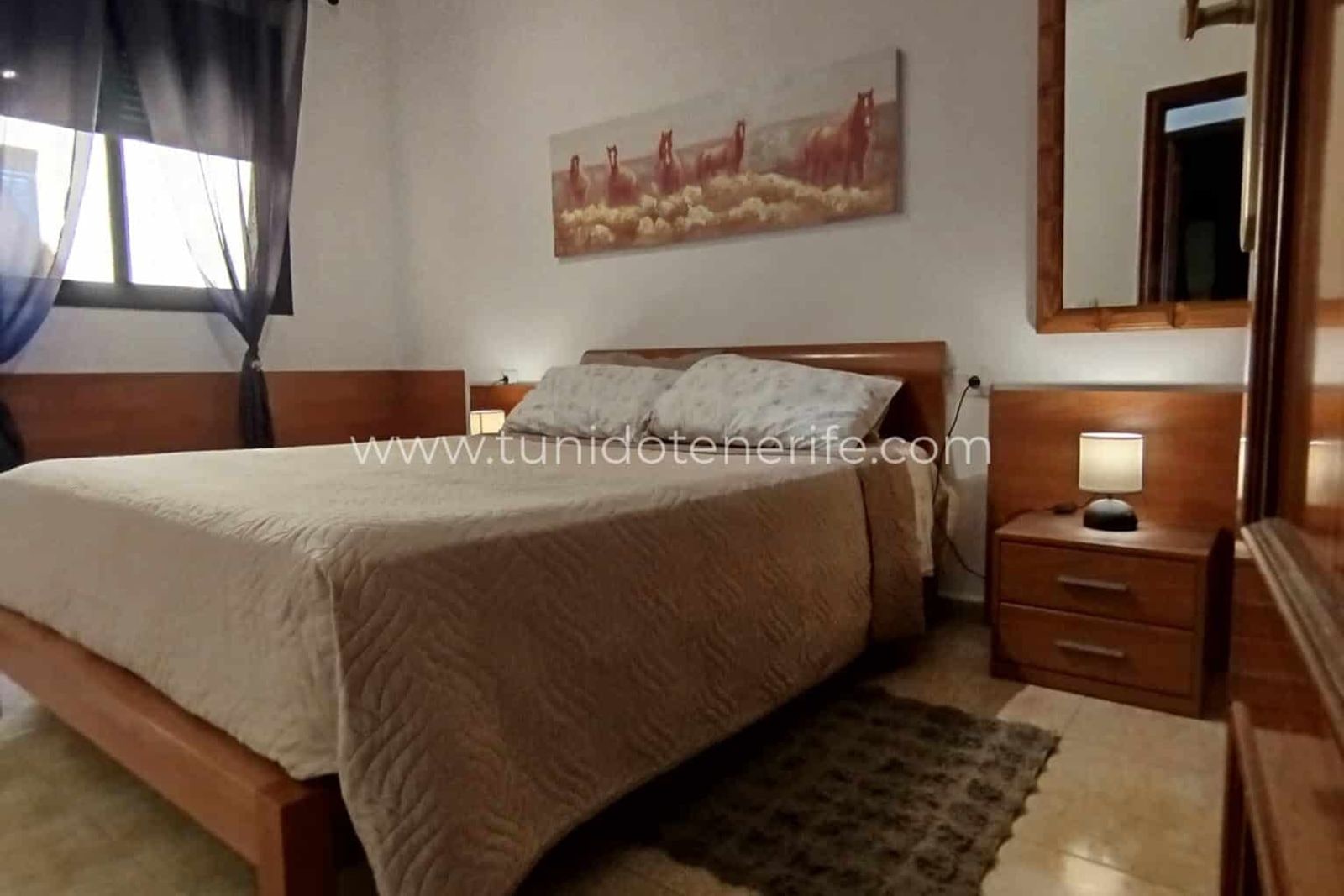 Dormitorio con cama doble, mesitas de noche, espejo y lámpara